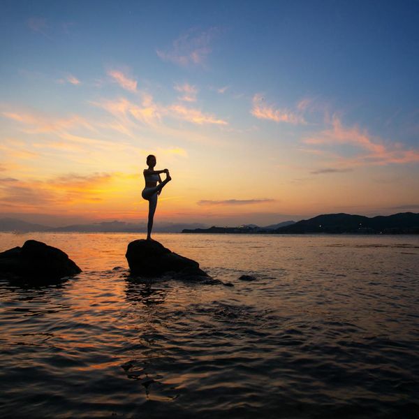 Person in a calm stretching pose outdoors at sunrise.